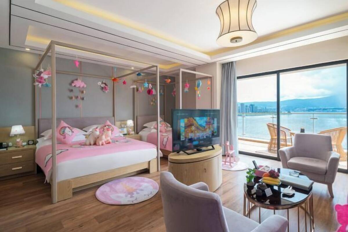 A modern hotel room with a large bed, a TV, a balcony with a view, and a dining area.