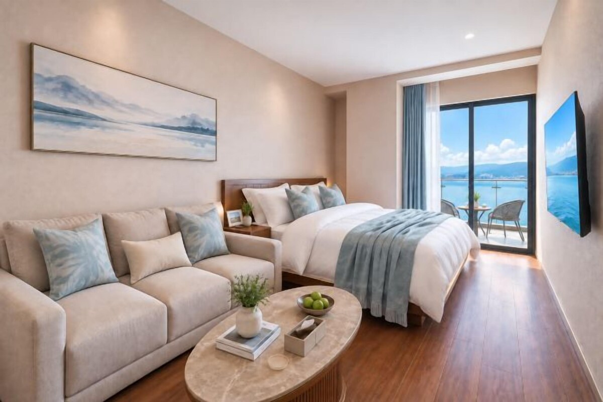 A modern hotel room with a bed, a sofa, a coffee table, and a view of the sea.