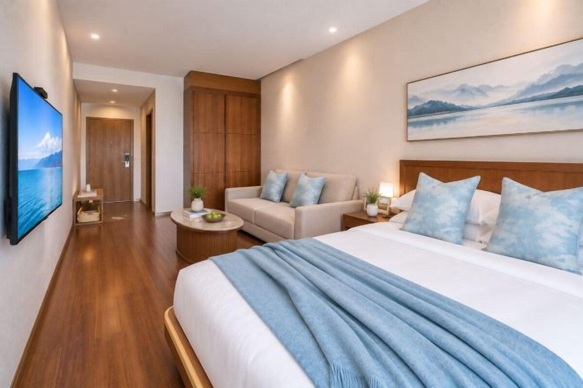 A hotel room with a bed, a sofa, a TV, and a painting on the wall.
