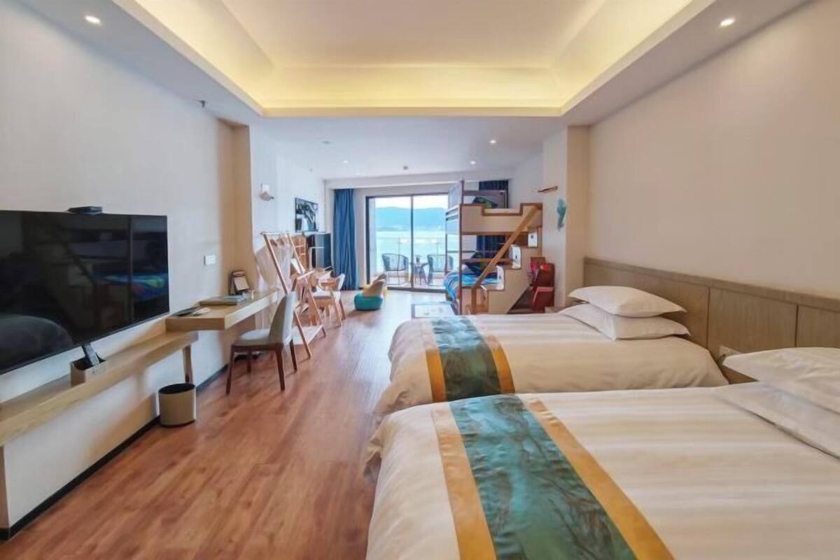A hotel room with a TV, two beds, a desk, and a view of the sea.