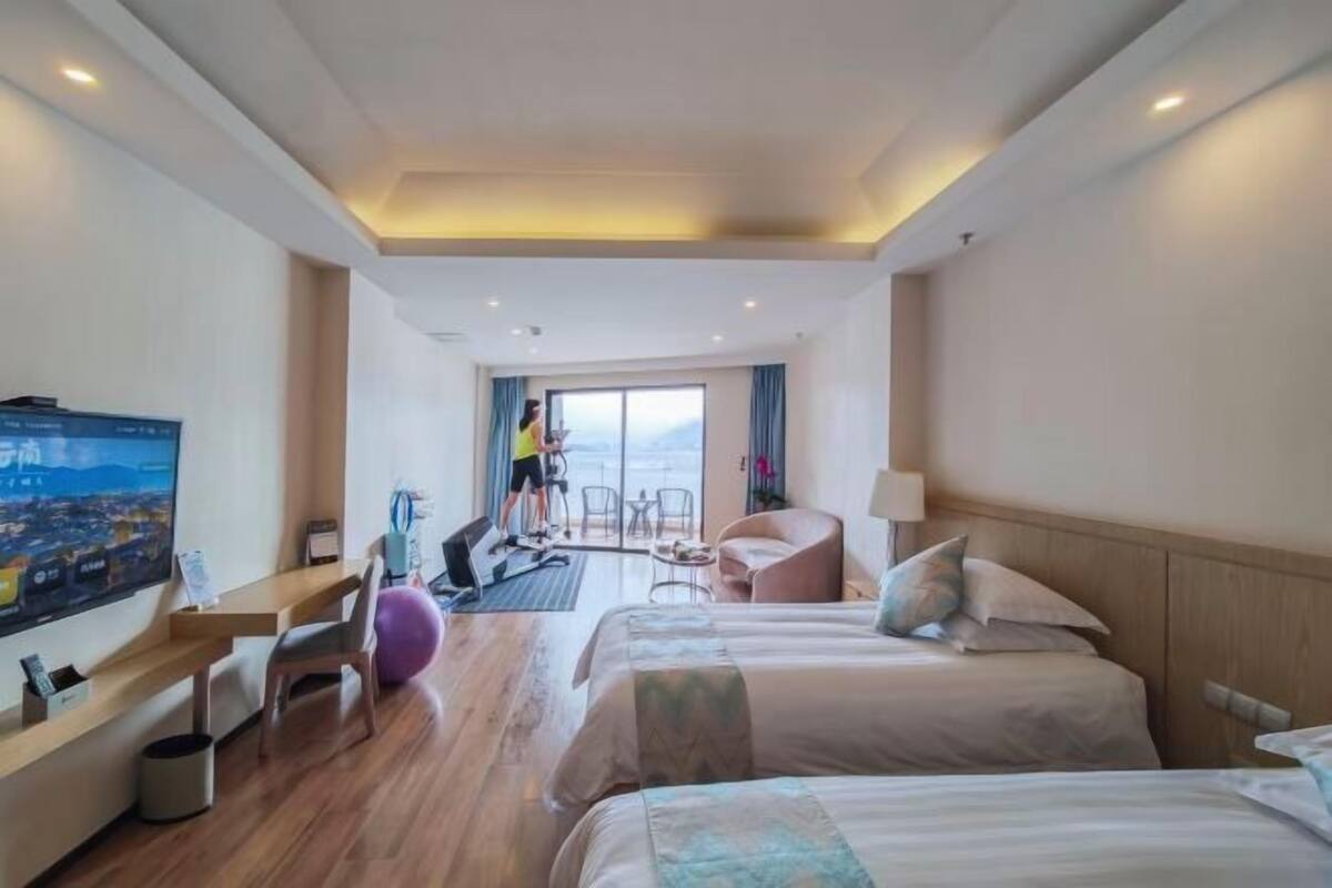 A hotel room with two beds, a TV, exercise equipment, and a view of the city.
