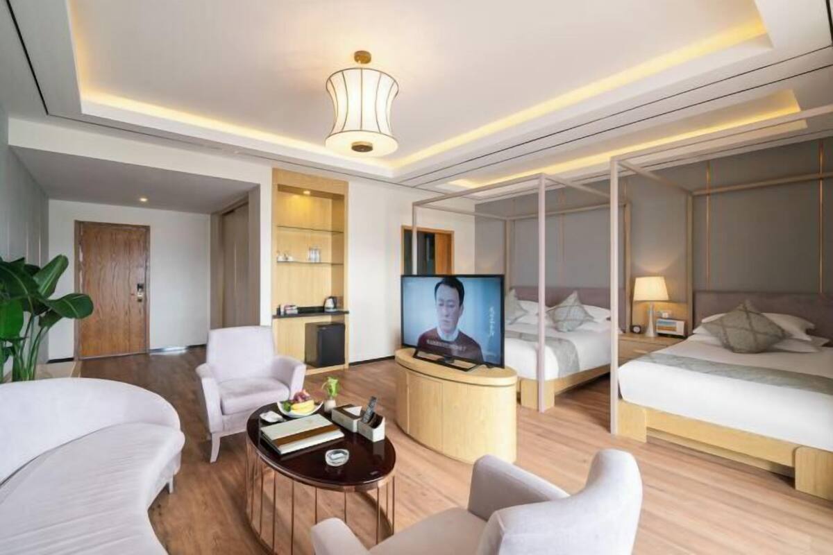 A modern hotel room with a curved sofa, a small round table, a TV, and a bed with a headboard.
