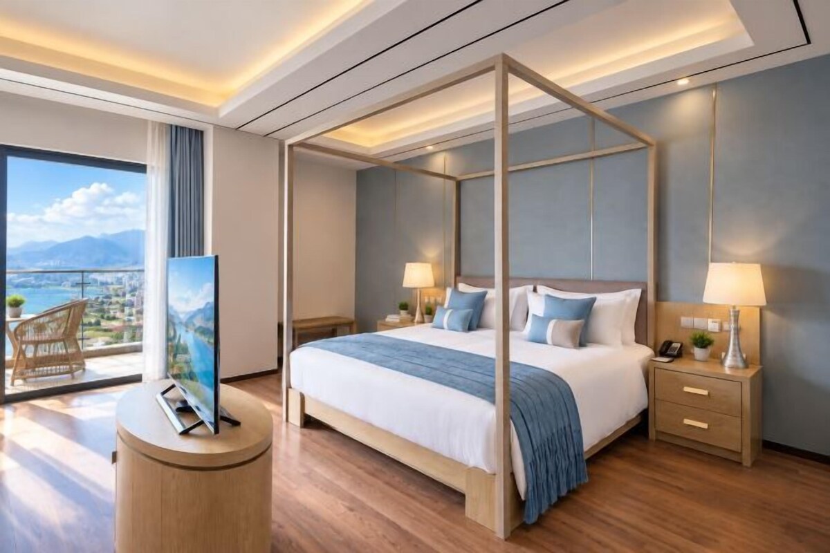 A four-poster bed with a view of the city, a round wooden side table, and a nightstand with a lamp.