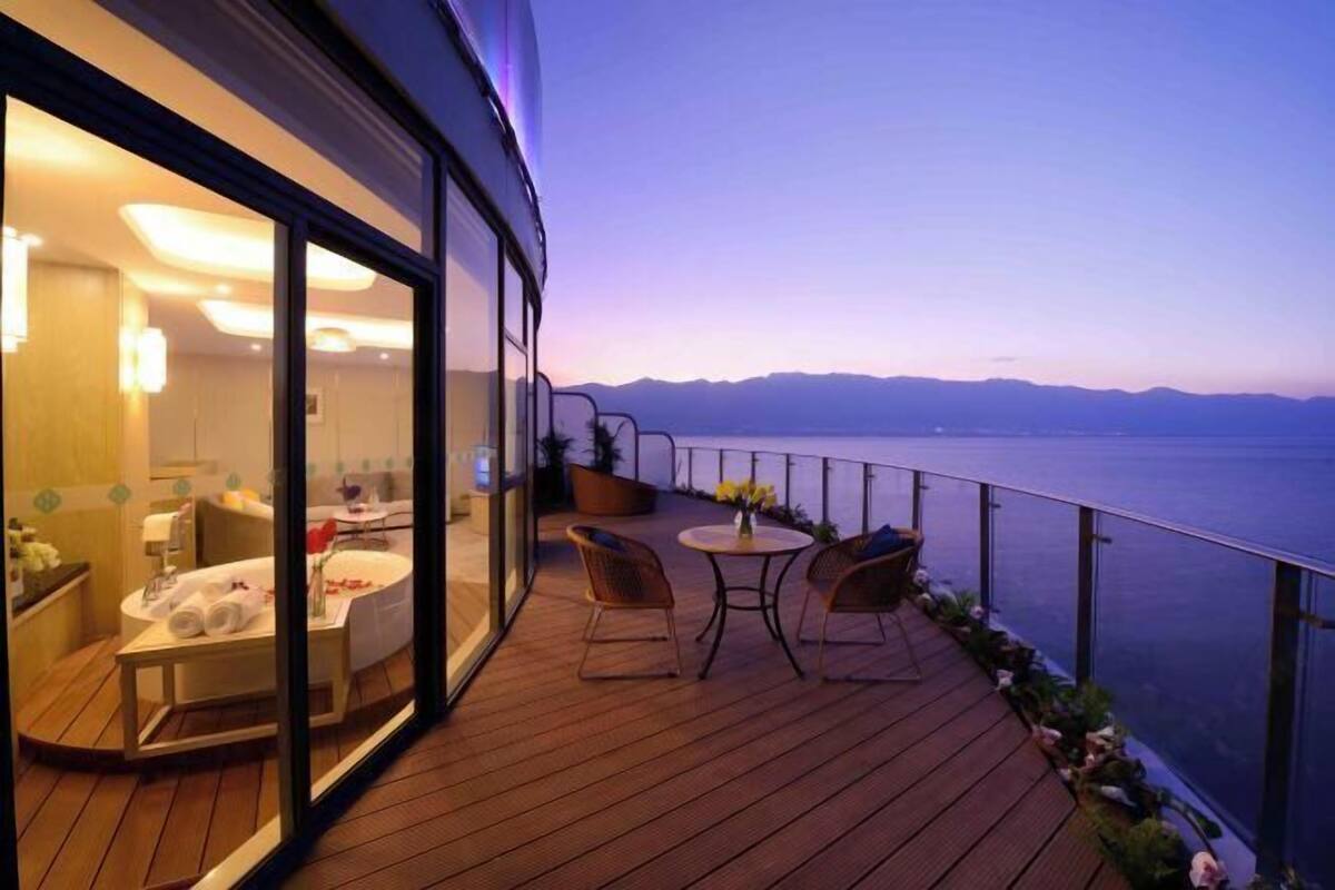 A deck with a view of the sea, a glass-enclosed room with a bathtub, and a table with chairs.
