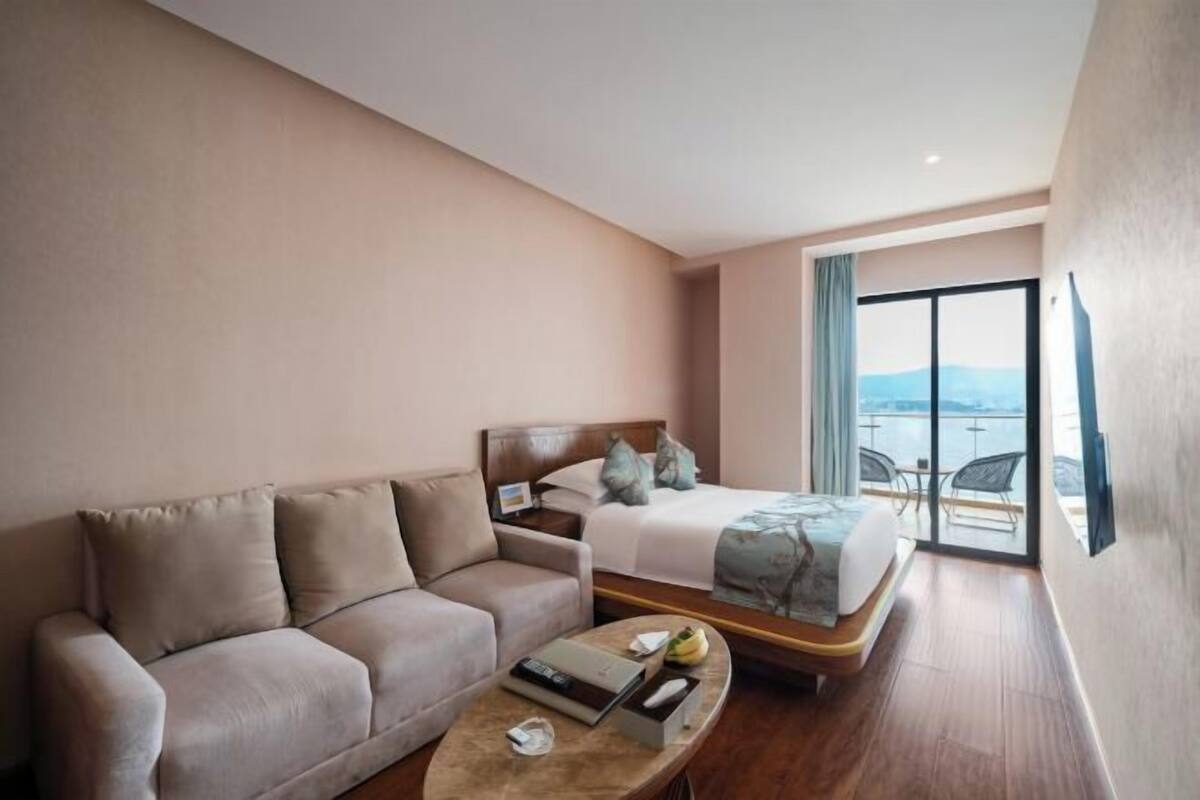 A hotel room with a sofa, a bed, a coffee table, and a view of the sea.
