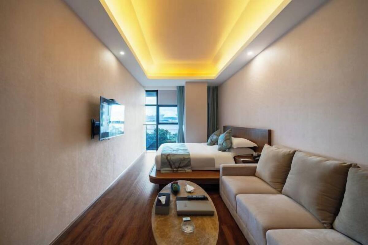 A modern hotel room with a bed, sofa, and a television mounted on the wall.