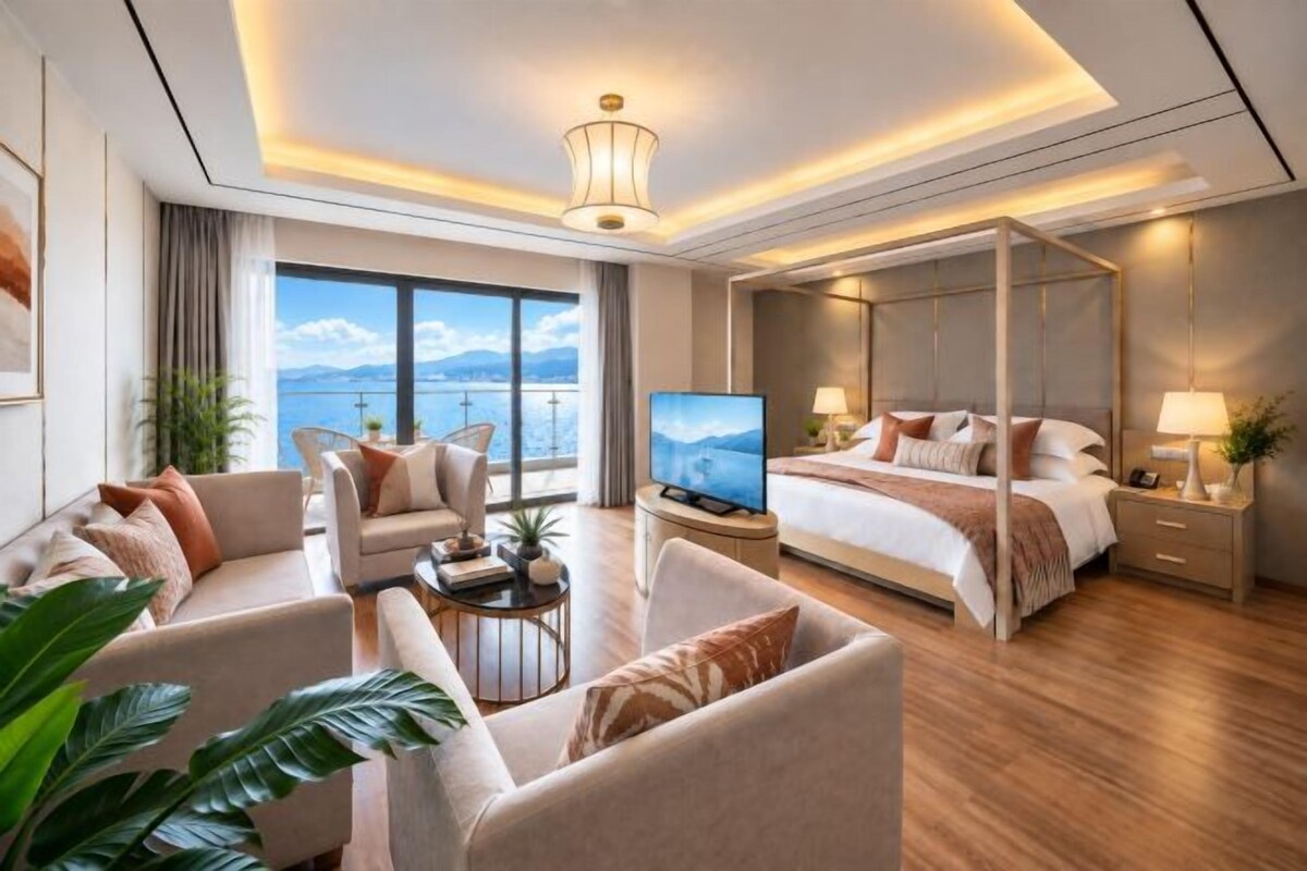A modern hotel room with a large bed, a sofa, a TV, and a balcony with a view of the sea.