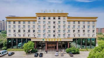 A multi-story hotel with a central entrance, surrounded by parked cars and greenery.
