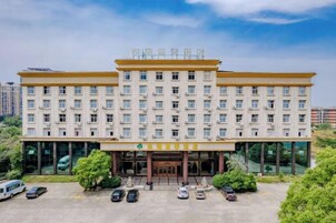 Un hotel de varios pisos con una entrada central, rodeado de coches aparcados y vegetación.