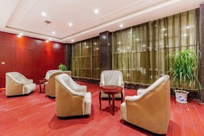 A hotel lobby with leather armchairs, a small table, and a potted plant.