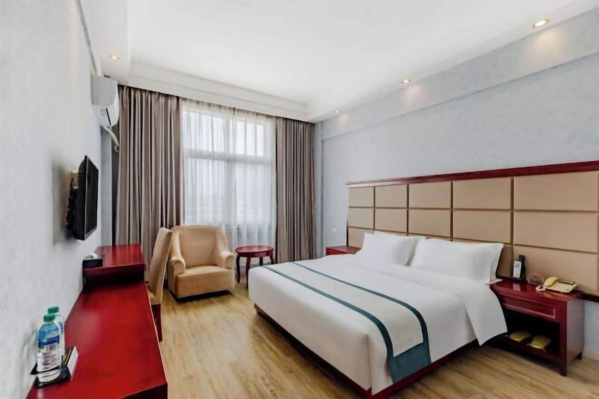 Une chambre d’hôtel avec un lit, une chaise, une petite table, une télévision et un bureau avec une bouteille et des verres.