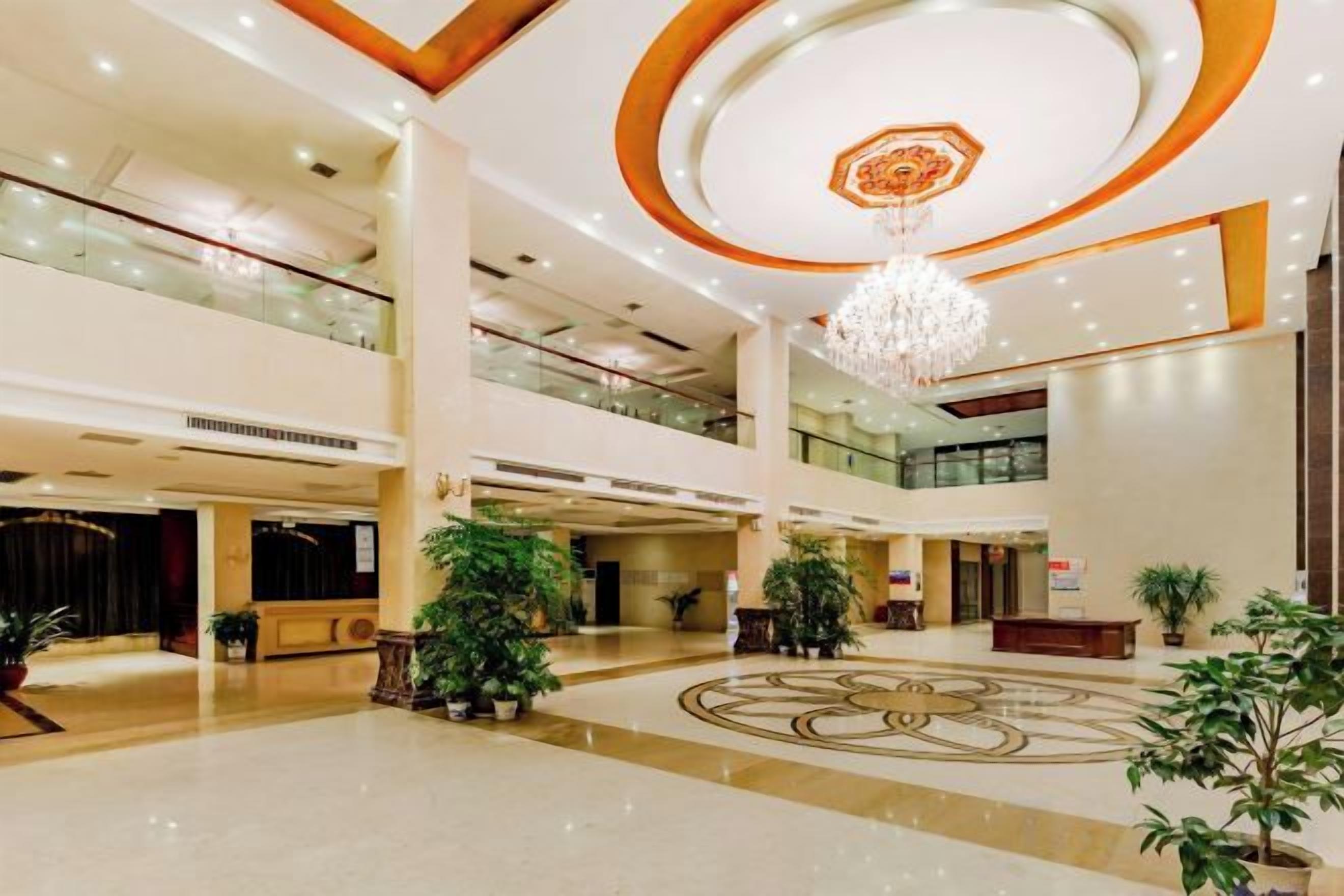 A spacious lobby with a chandelier, multiple floors, and potted plants.
