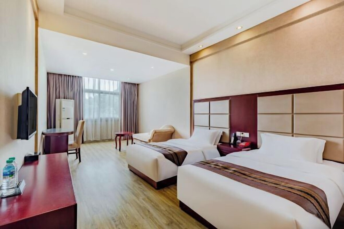 A hotel room with two beds, a desk, a chair, a TV, and a window with curtains.