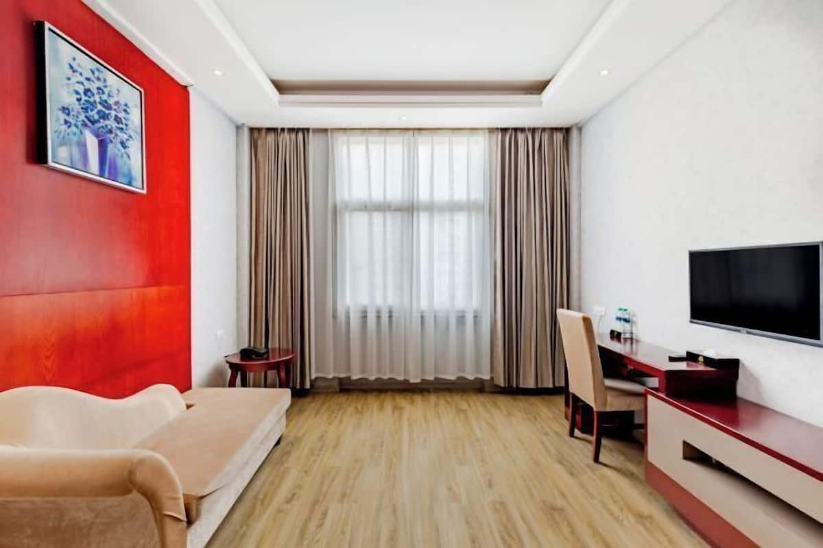 Une chambre d’hôtel avec un mur d’accent rouge, une grande fenêtre avec des rideaux, un téléviseur à écran plat, un canapé et un bureau avec une chaise.