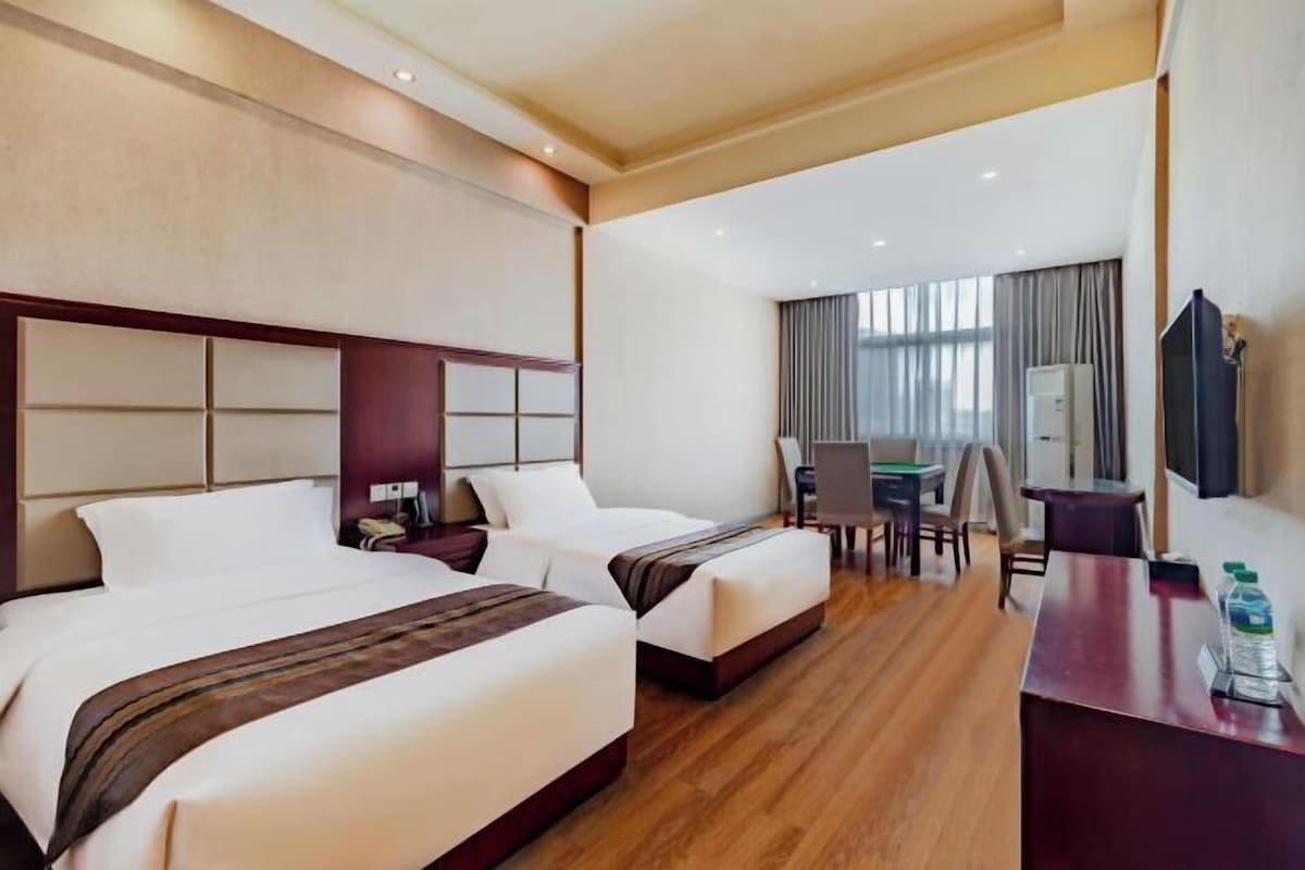 A hotel room with two beds, a desk, a chair, a TV, and a window with curtains.
