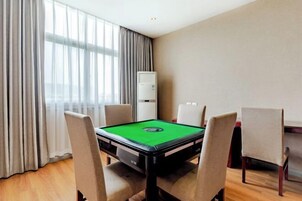 Una habitación con mesa de billar, cuatro sillas, un ventanal con cortinas y un equipo de aire acondicionado blanco.