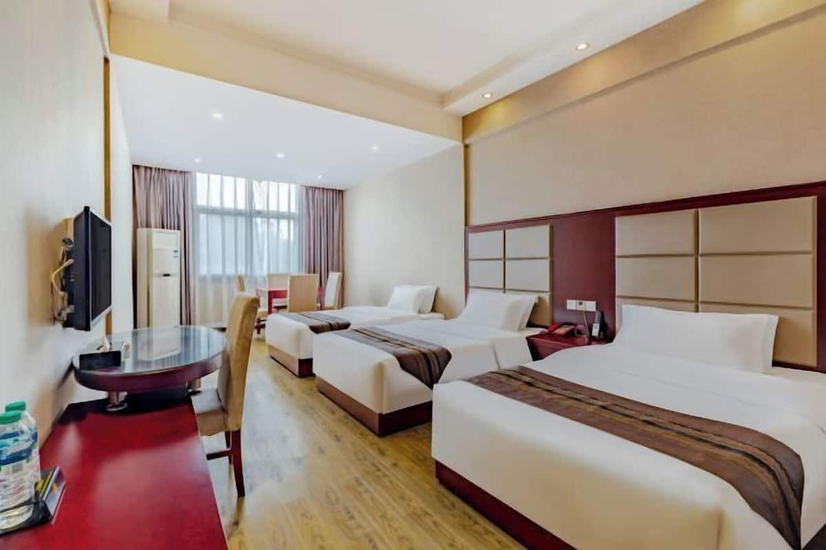 Une chambre d’hôtel avec deux lits, un bureau, une chaise, une télévision et une fenêtre avec des rideaux.