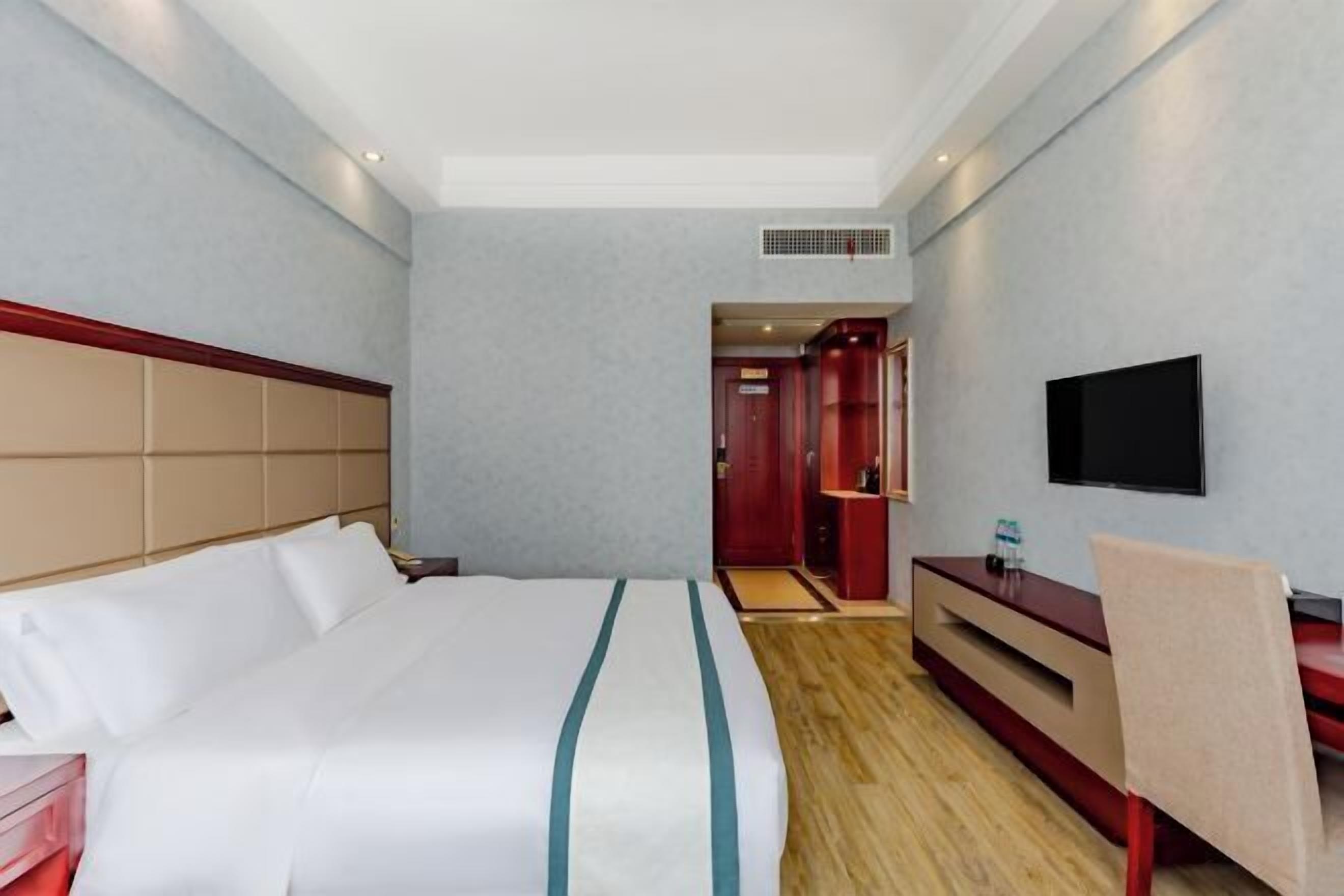 Ein Hotelzimmer mit Bett, Fernseher, Schreibtisch und einem roten Kleiderschrank.