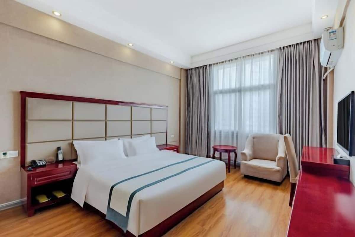 Une chambre d’hôtel avec un grand lit, une table de chevet, une chaise, une petite table et un téléviseur.