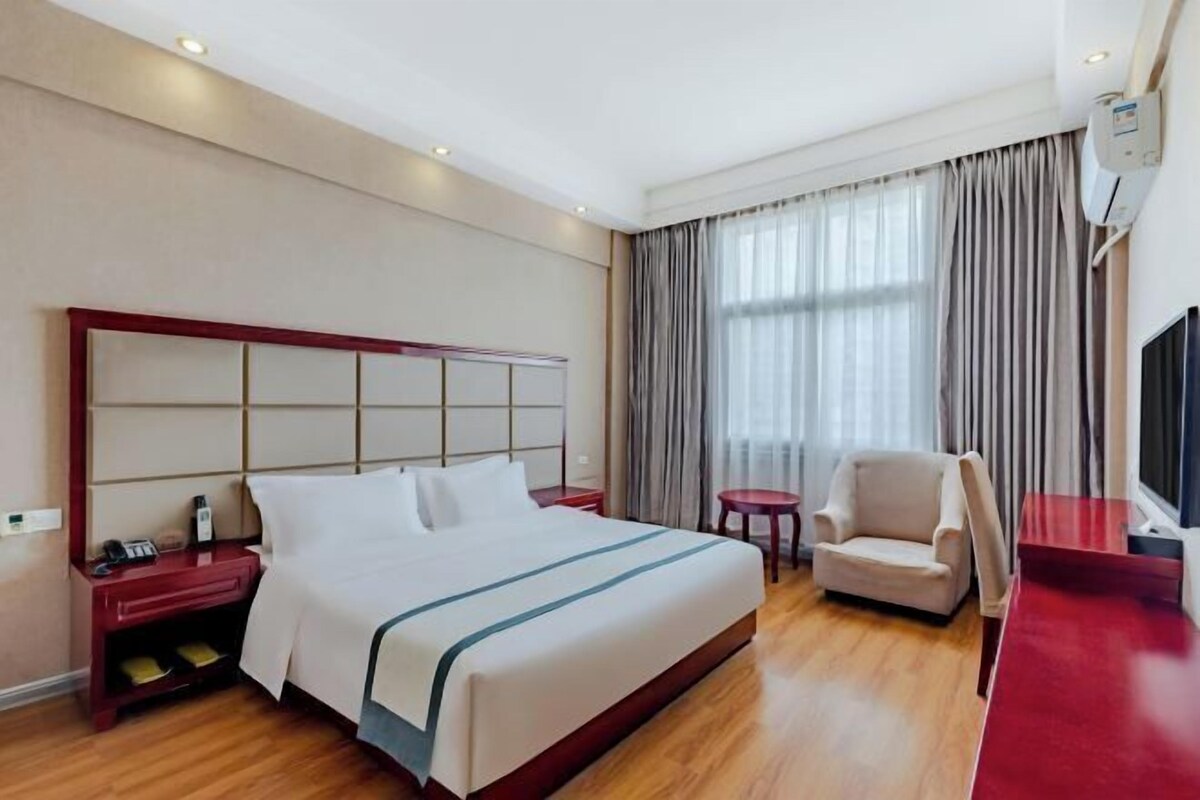 A hotel room with a large bed, a desk, a chair, a TV, and a window with curtains.