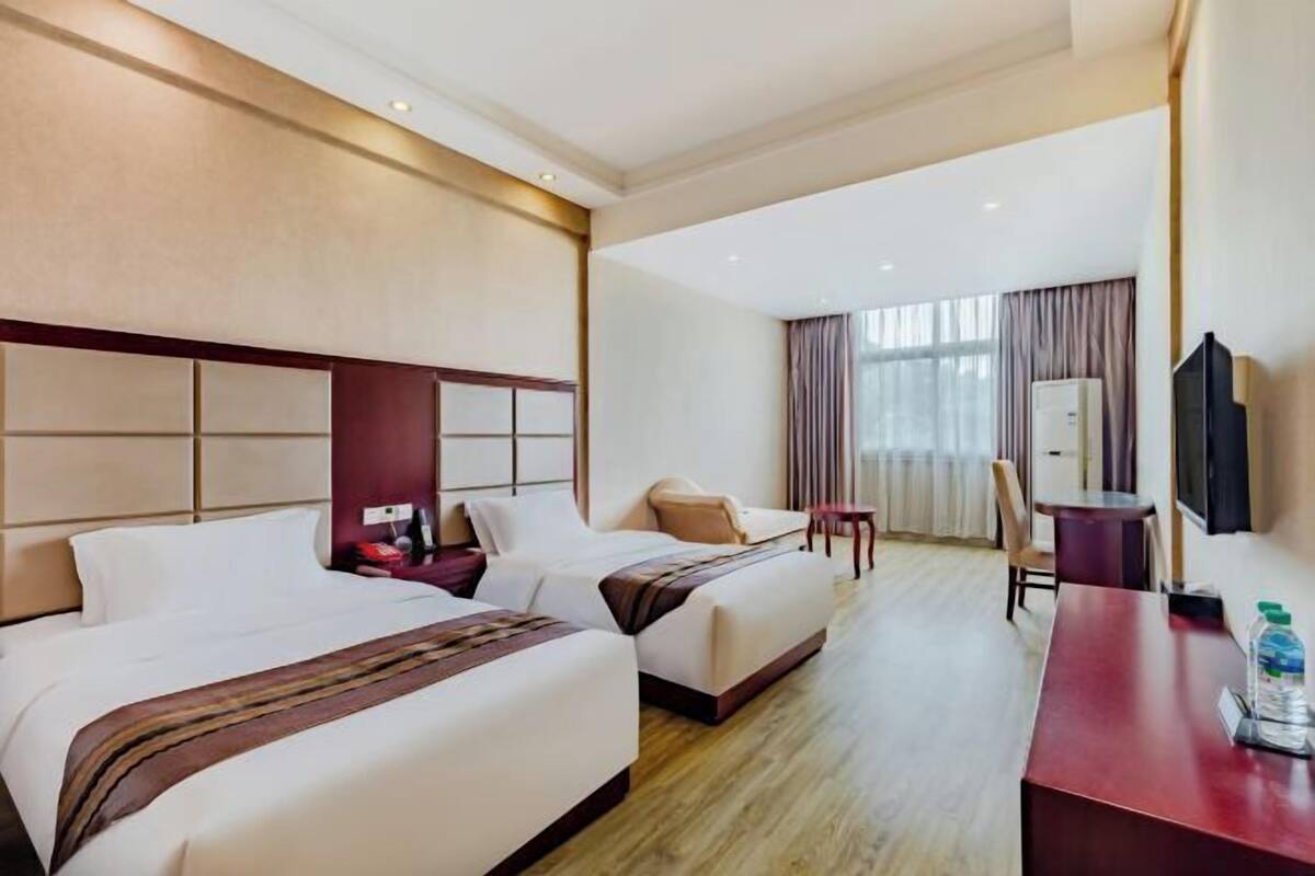 Une chambre d’hôtel avec deux lits, un bureau, une chaise, une télévision et une fenêtre avec des rideaux.