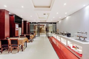 Une salle à manger d’hôtel avec des tables et des chaises, un buffet où sont présentés les plats, et une vue dégagée sur l’entrée.