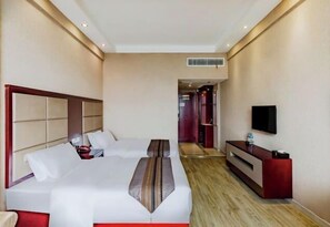 Ein Hotelzimmer mit zwei Betten, einem Fernseher, einem Schreibtisch und einem begehbaren Kleiderschrank.