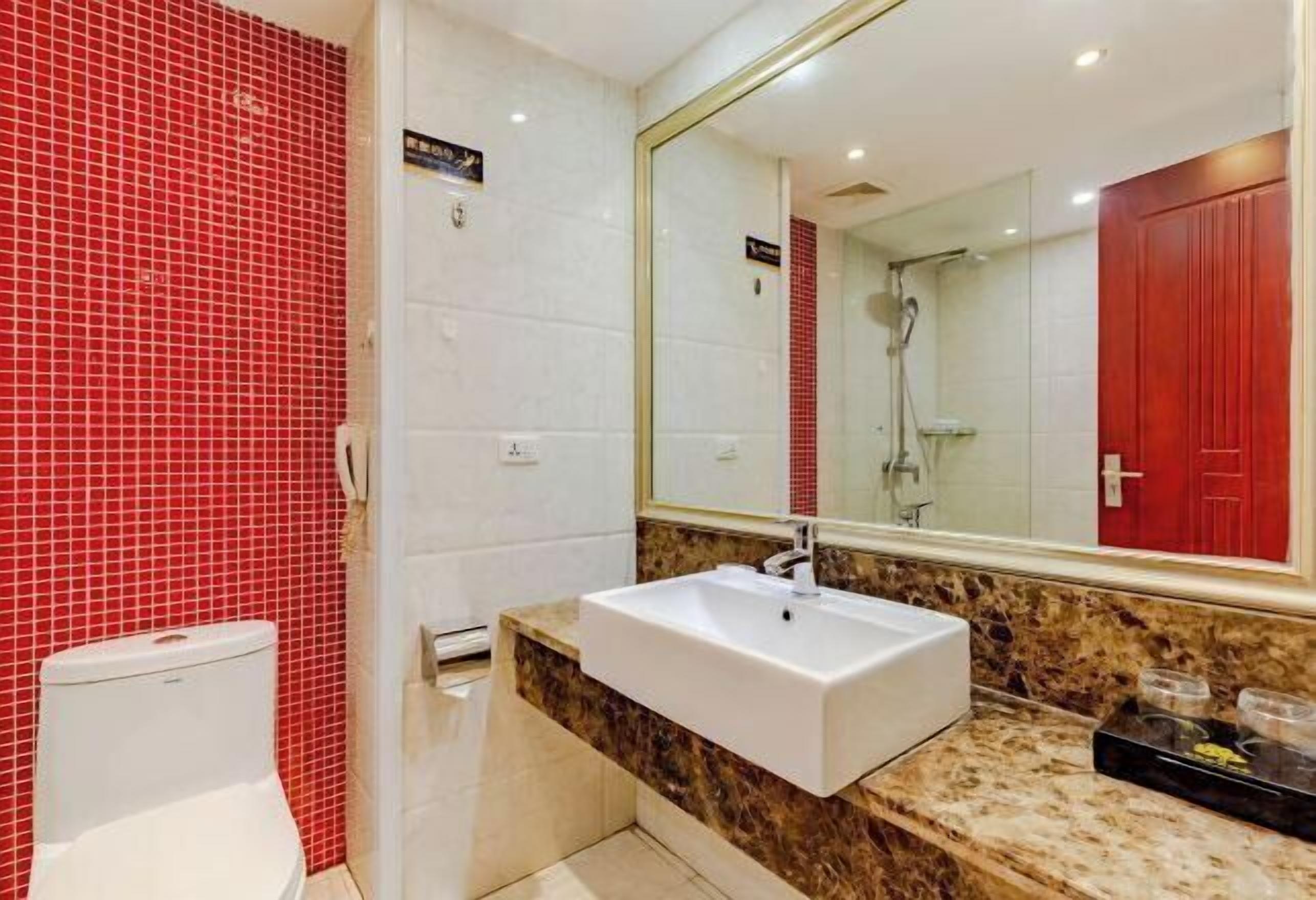 A bathroom with a white sink, red tiled walls, and a large mirror.