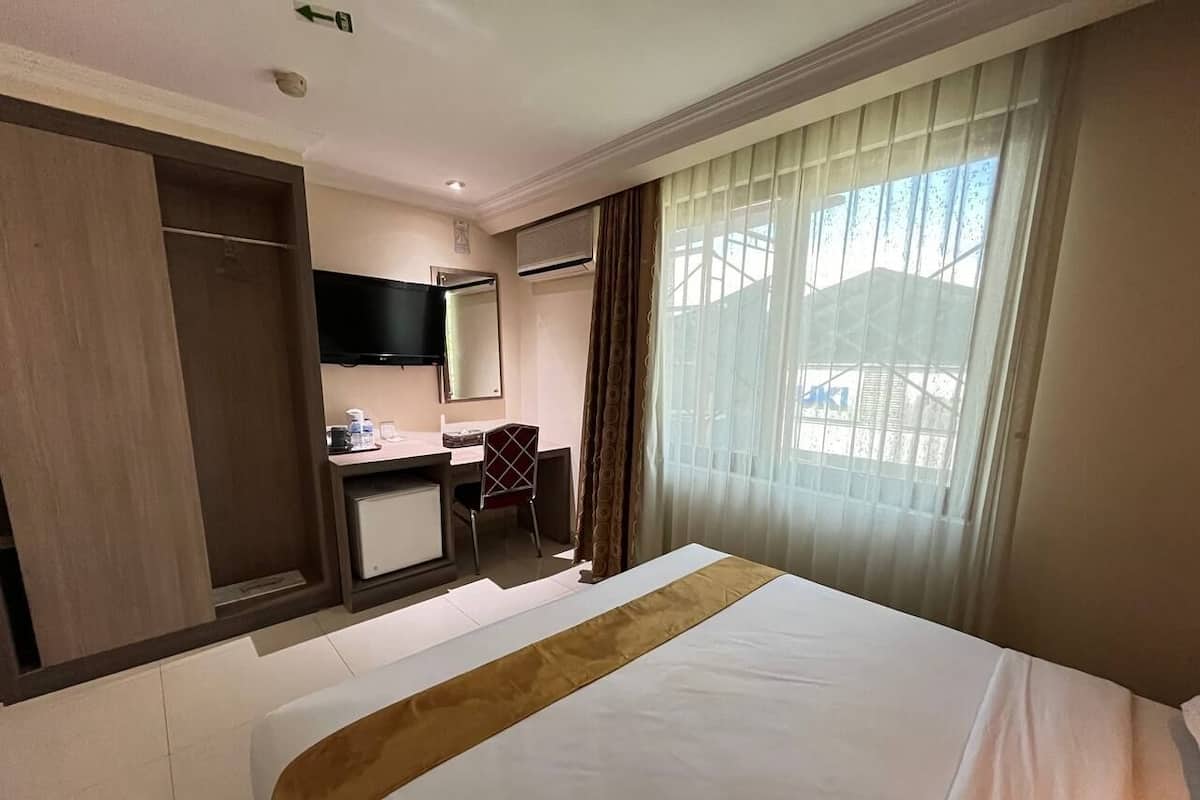 A hotel room with a bed, a desk, a chair, a TV, and a window with curtains.