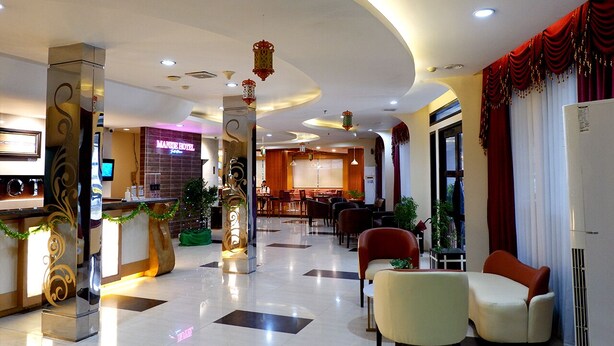 Un vestíbulo de hotel con mostrador de recepción, zona de estar y un bar/sala de estar al fondo.