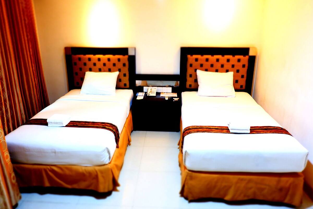 A hotel room with two single beds, a small table, and a nightstand.
