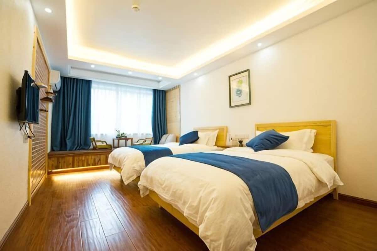 Habitación de hotel con dos camas, televisión, ventana con cortinas y suelo de madera.