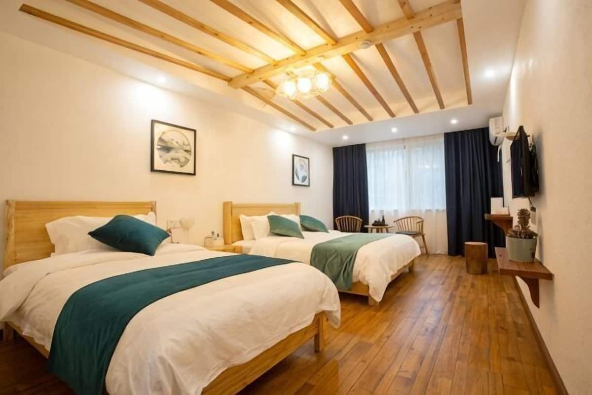Habitación de hotel con dos camas, vigas de madera en el techo, una ventana con cortinas y una pequeña mesa con una silla.