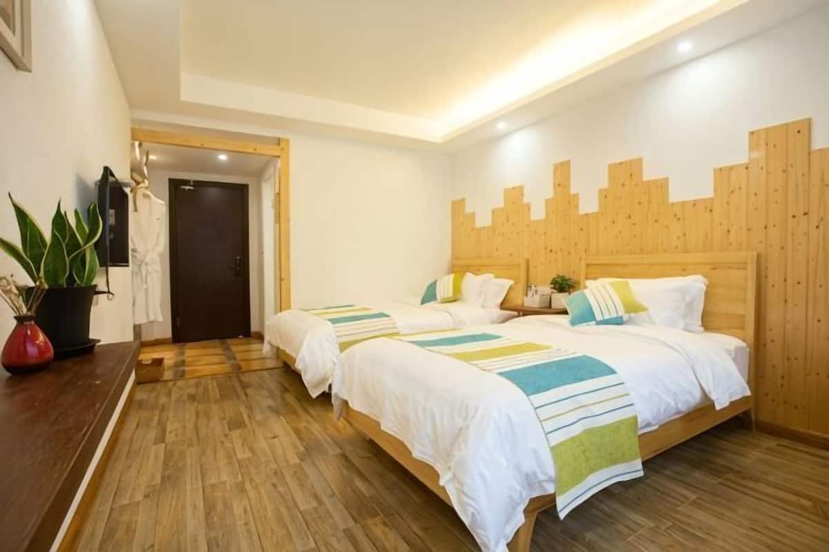 Una habitación con dos camas, cabeceros de madera, piso de madera, una mesita con una planta y una puerta.