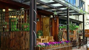 Une façade en bois avec une base en briques, une véranda couverte avec des meubles en bois et des plantes en pot.