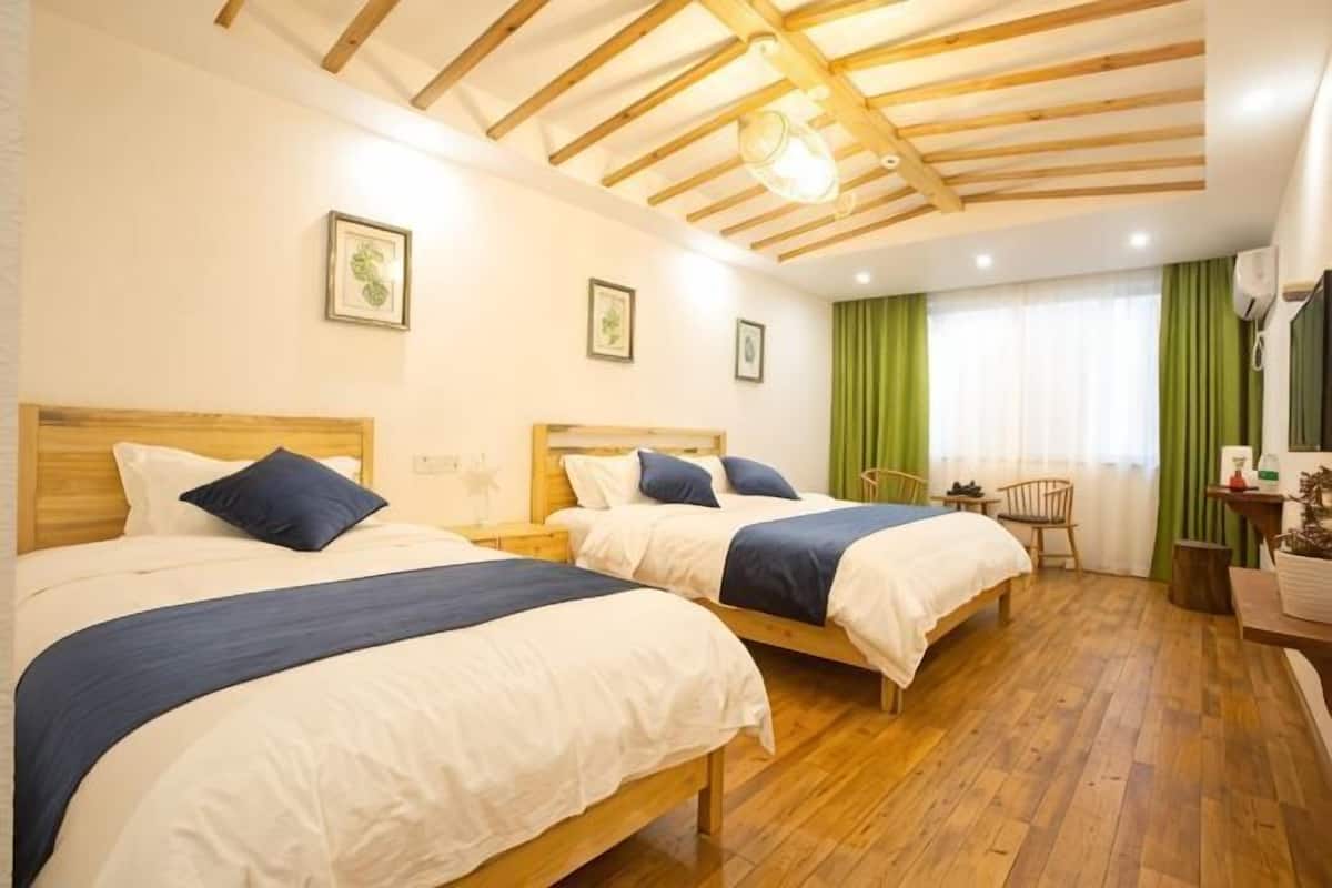 Habitación de hotel con dos camas, piso de madera, cortina verde y techo de madera.