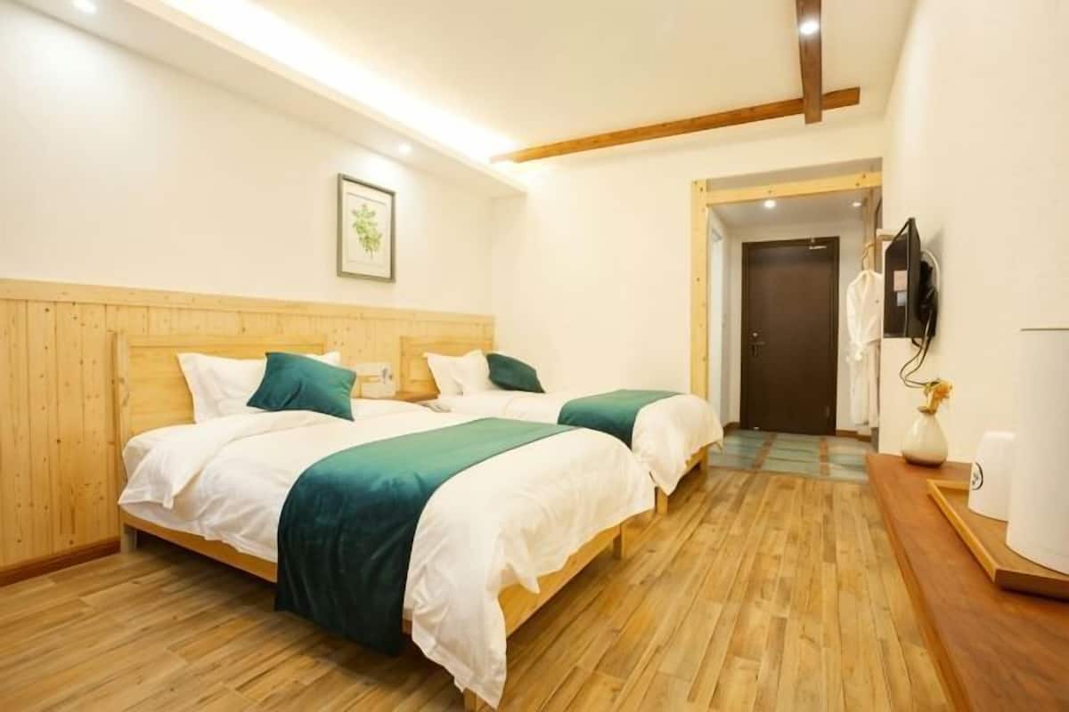 Una habitación con dos camas, suelo de madera, un cuadro enmarcado en la pared, una puerta y una mesita con un florero.