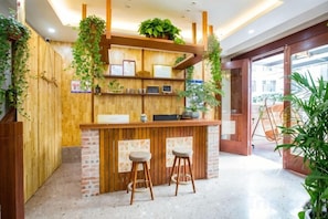 Un espace d’accueil avec un comptoir en bois, deux tabourets de bar et une plante suspendue.
