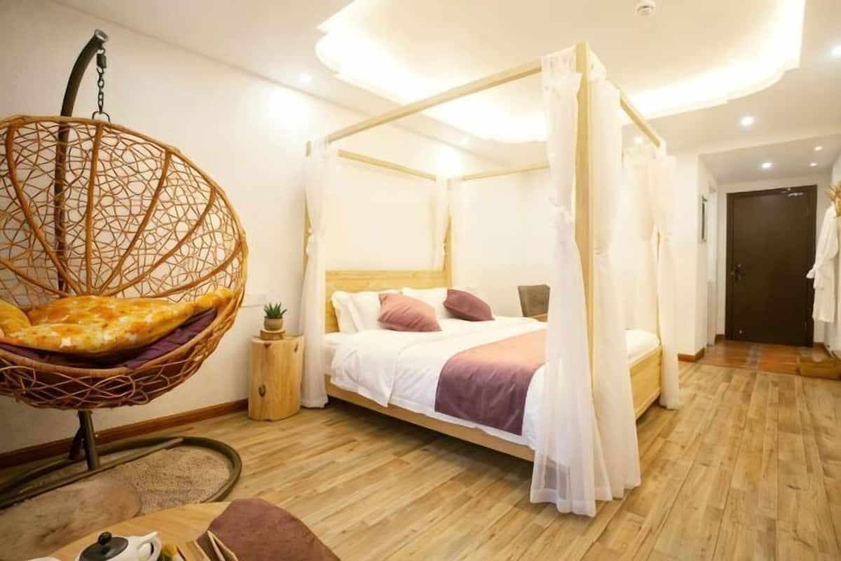 Un dormitorio con una silla colgante, una cama con dosel y suelo de madera.
