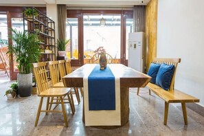 Un coin repas avec une table en bois, des chaises et un banc. On aperçoit une bibliothèque et une plante en pot à l’arrière-plan.