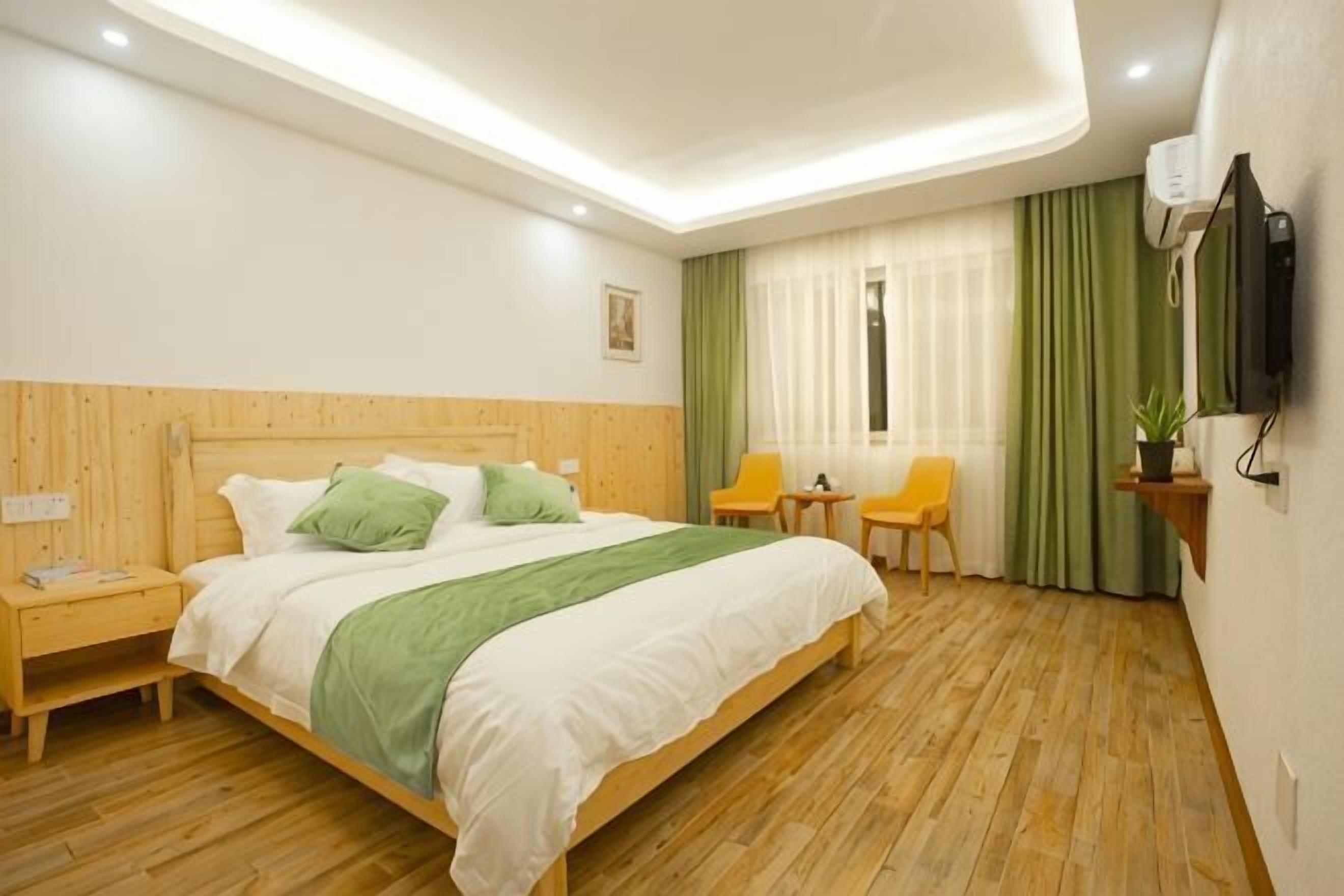 Una camera d'albergo con un letto in legno, un comodino, una sedia, un tavolino, una TV e una finestra con tende.