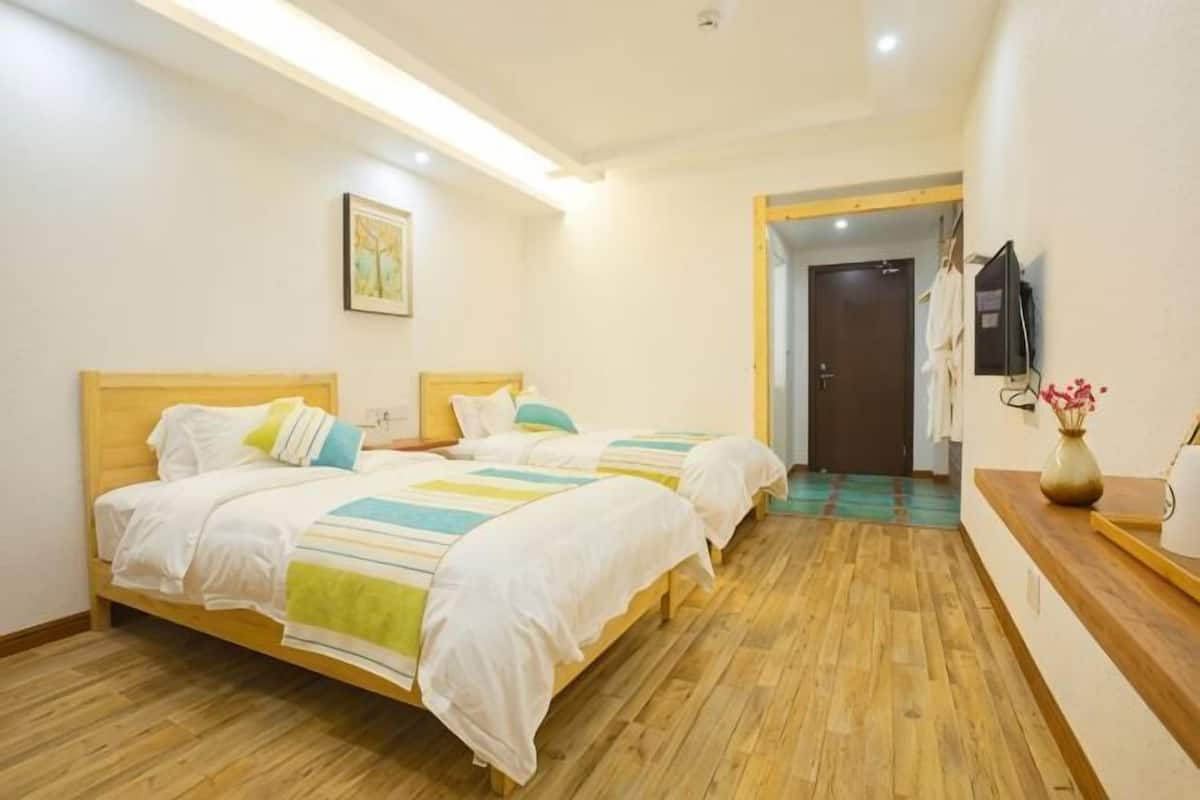 Habitación de hotel con dos camas, piso de madera, un cuadro en la pared y un televisor en la pared.