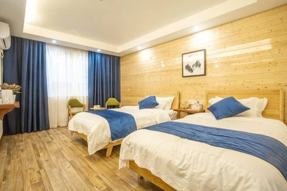 Habitación de hotel con dos camas, suelo de madera, un escritorio con silla y un ventanal con cortinas.
