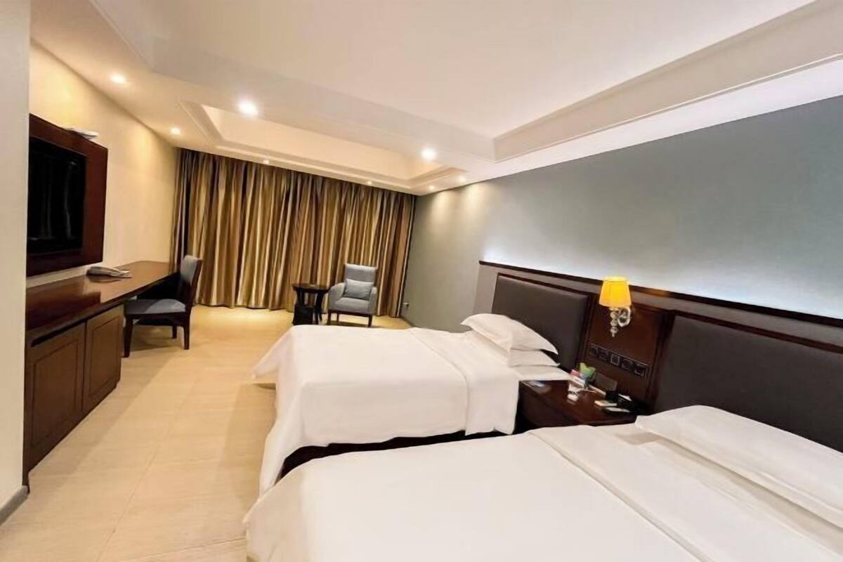 Habitación de hotel con dos camas, un escritorio, un televisor y una silla.