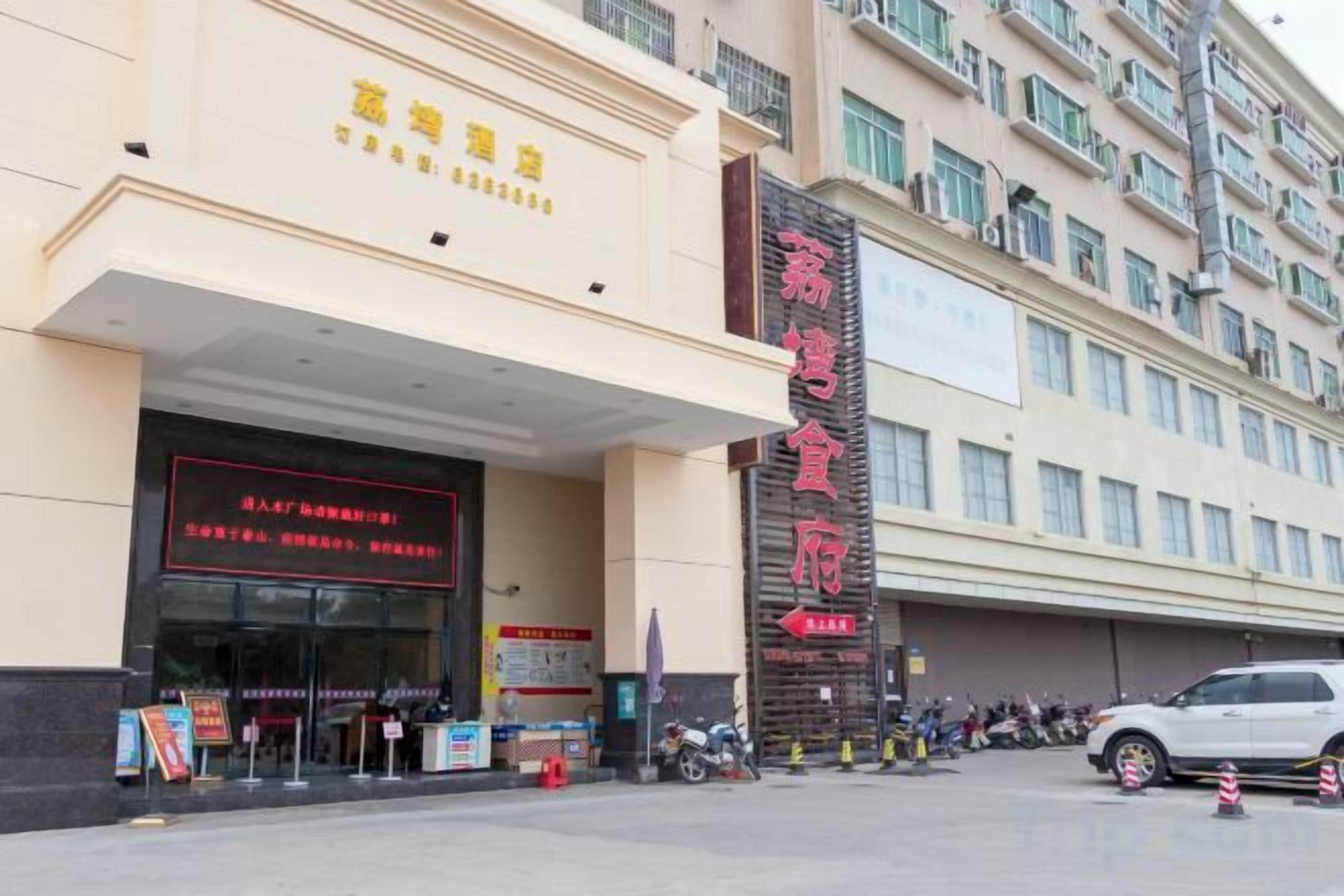 A hotel entrance with a prominent sign, a covered entrance area, and a parking lot with vehicles.