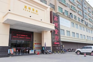 A hotel entrance with a prominent sign, a covered entrance area, and a parking lot with vehicles.