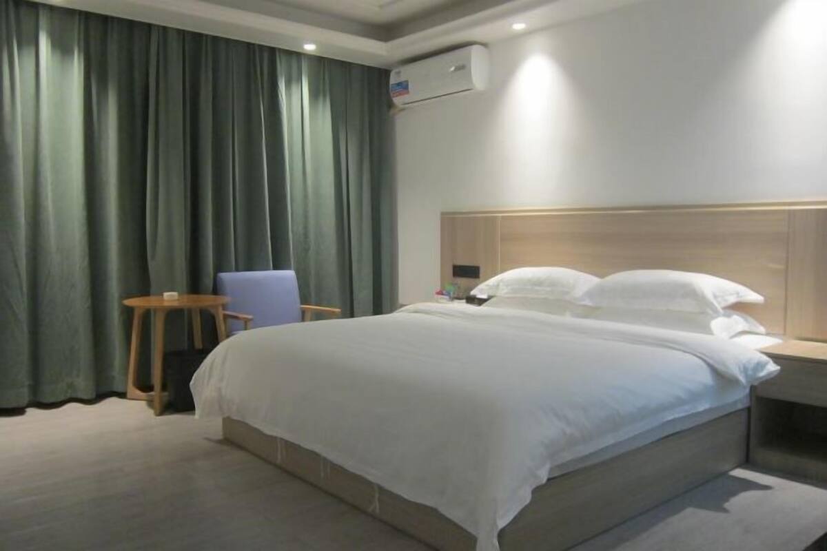 Una habitación de hotel con cama, una silla, una mesita y aire acondicionado instalado en la pared.