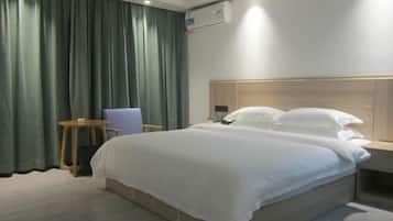 A hotel room with a bed, a chair, a small table, and a wall-mounted air conditioner.