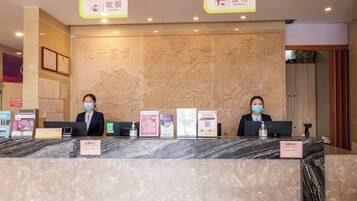 A reception desk with two staff members, a marble counter, and informational signs.