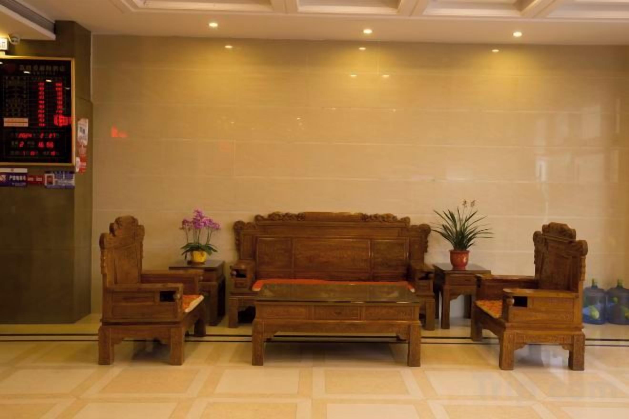 Un vestíbulo con un sofá de madera, dos sillones, una mesita de centro y una pequeña mesa con una planta.